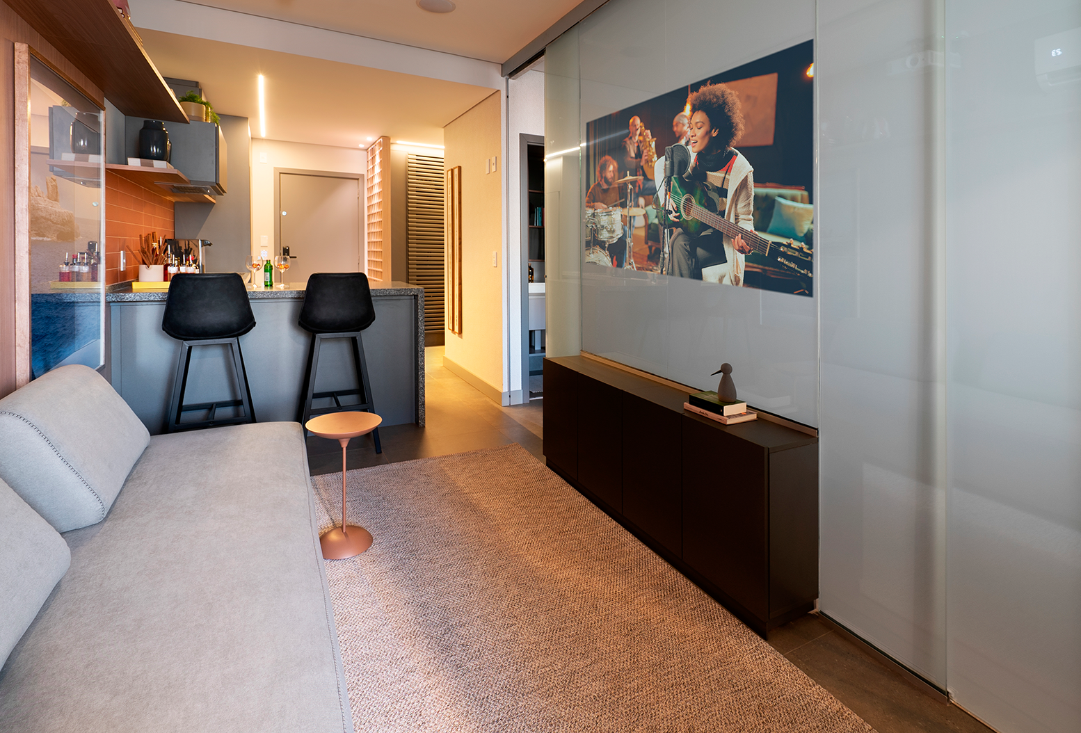 Espaço decorado com estilo contendo sala de TV, cozinha ao fundo e quarto ao lado, próximos e bem integrados.