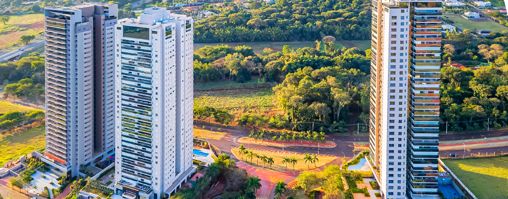 Visão aérea de torres de condomínio e bastante verde ao redor, com ruas e calçadas bem definidas, além de paisagismo nas torres.