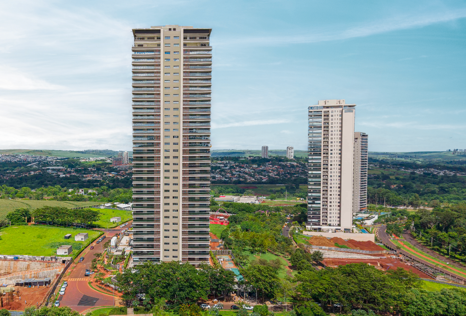 Vista aérea de um prédio alto e moderno, cercado por ruas, áreas verdes e a cidade ao fundo.