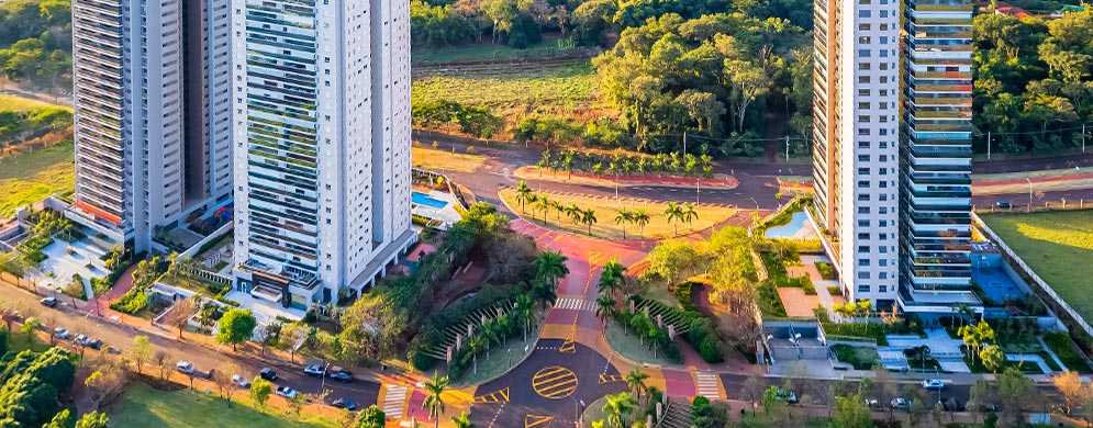 Visão aérea de torres de condomínio e bastante verde ao redor, com ruas e calçadas bem definidas, além de paisagismo nas torres.