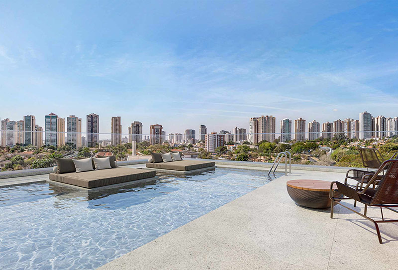 Piscina na cobertura com espreguiçadeiras, poltronas e vista panorâmica da skyline de Ribeirão Preto.