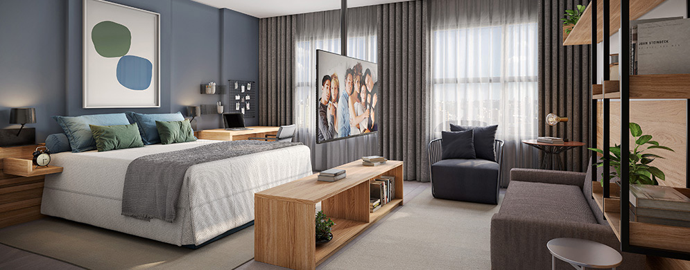 Studio com cama, sofá, poltrona, TV giratória, bancada de trabalho e grandes janelas com cortinas.