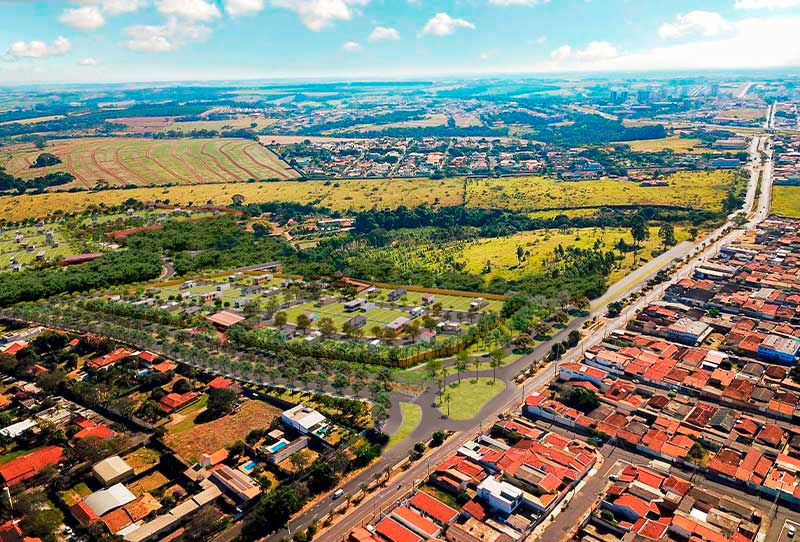 Visão aérea de grande espaço verde com os lotes disponíveis para venda, com rodovia de acesso e bairro residencial próximo. 